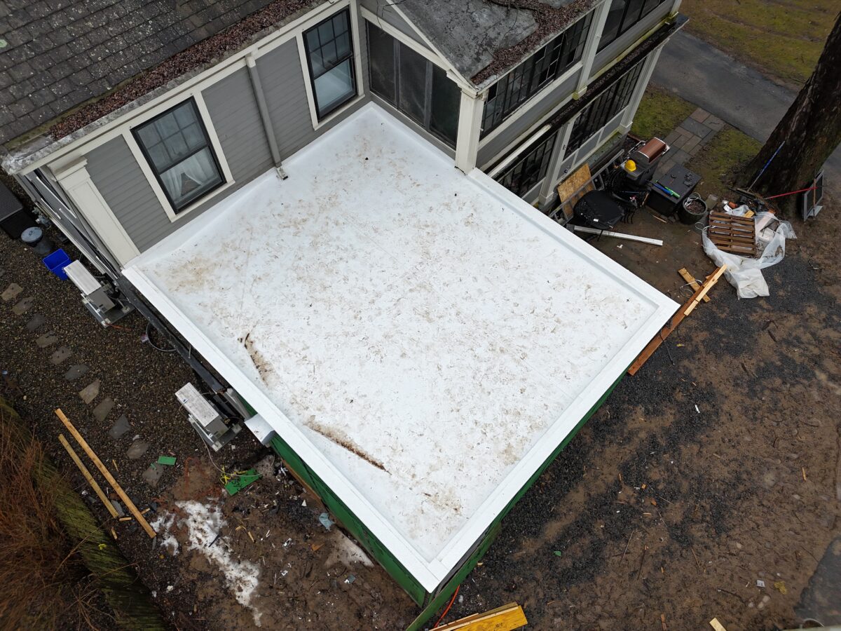 Aerial view of a new white membrane flat roof on a one-story addition attached to a gray-sided house