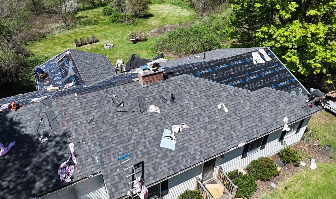 Crew installing new architectural shingles over ice barrier and underlayment on a ranch home roof