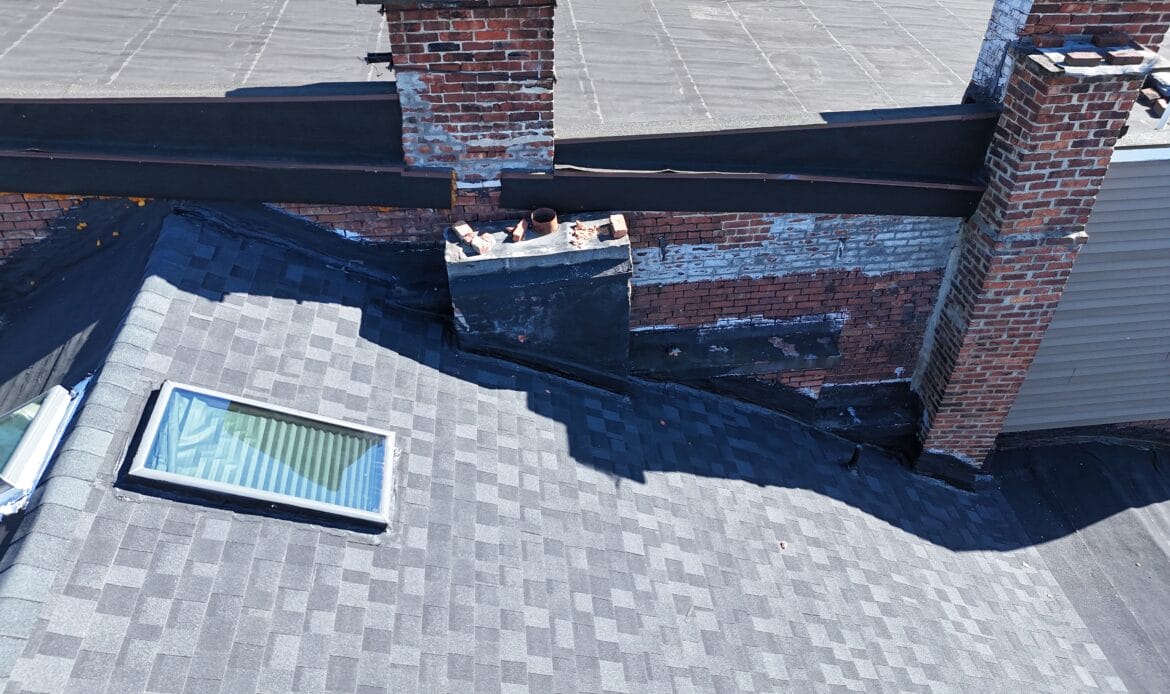 Aerial view of a skylight in a gray asphalt shingle roof beside brick chimneys on a Capital Region home