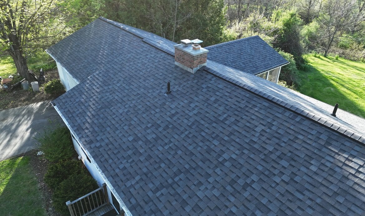 Close aerial view of a new gray architectural shingle roof with a brick chimney and ridge vent